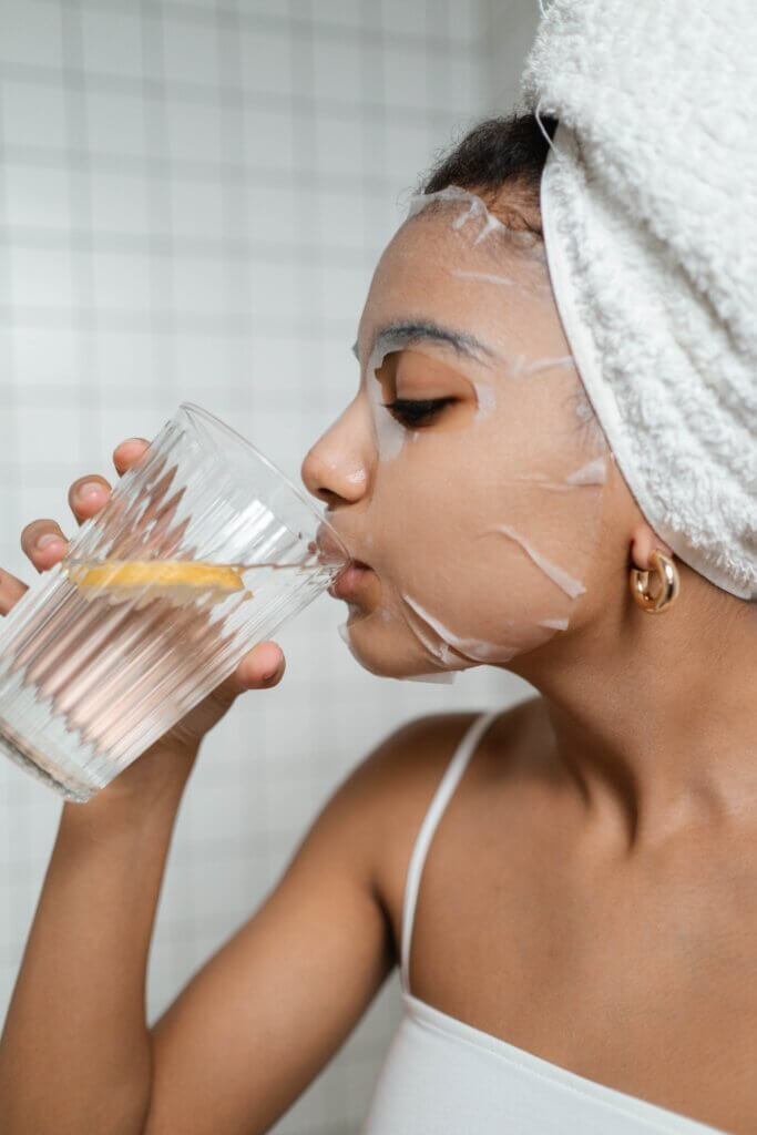 woman doing face maask and drinking water